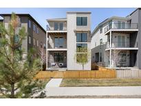Modern three-story home featuring private balconies, stone accents, and a wooden fence, enhancing curb appeal at 21418 E 61St Dr, Aurora, CO 80019