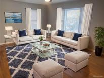 Inviting living room with hardwood floors, plush rug, white sofas, and a modern glass coffee table at 1180 Walnut St, Brighton, CO 80601