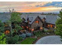 Luxury home featuring a manicured lawn, stone patio, with seating and a colorful mountain sunset at 4030 E Forbes Ct, Greenwood Village, CO 80121