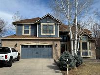 Charming two-story home featuring brick and blue siding, an attached garage, and mature trees in the front yard at 1618 Garnet St, Broomfield, CO 80020