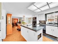 Bright kitchen featuring an island, white cabinets, black countertops and stainless steel appliances at 6005 S Jamaica Way, Englewood, CO 80111