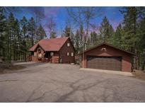 Charming cabin-style home with wood siding and a detached two-car garage nestled among trees at 9530 Aspen Ln, Conifer, CO 80433