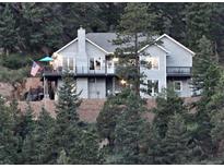 Charming gray two-story home nestled on a hill surrounded by lush trees and multiple decks at 83 Wilderness Cornerstone Rd, Evergreen, CO 80439