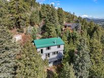 Two-story home with green roof nestled amongst the trees with a deck at 8386 S Davco Dr, Morrison, CO 80465