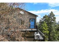 Gray two-story home with a blue door and black metal balcony, surrounded by trees at 8386 S Davco Dr, Morrison, CO 80465