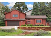 Charming two-story red home with lush landscaping and a two-car garage at 6293 Ponderosa Way, Parker, CO 80134