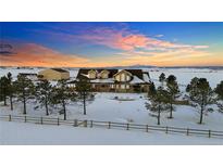 Scenic aerial view captures a charming home embraced by snow-covered landscaping and an expansive open field at 4075 Merada Ct, Franktown, CO 80116