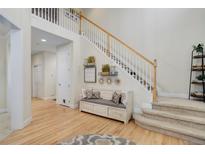 Inviting foyer featuring light wood floors, a staircase with white railings, and a cozy bench with decorative pillows at 12451 Turquoise Terrace Pl, Castle Pines, CO 80108