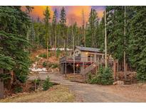 Charming mountain home with wrap-around deck nestled among tall evergreen trees at sunset at 34788 Forest Estates Rd, Evergreen, CO 80439