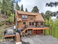 Charming two-story log home with a spacious deck, attached garage, and a hot tub surrounded by lush greenery at 1000 Lodgepole Dr, Evergreen, CO 80439