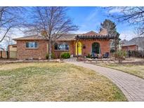 Charming brick home featuring a walkway to a pergola covered patio, a yellow door and a well-manicured lawn at 2576 Krameria St, Denver, CO 80207