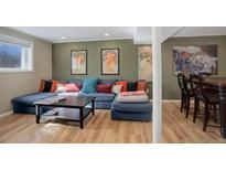 Finished basement featuring a large sectional sofa, stylish artwork, and a cozy bar area with modern wood floors at 15541 E Cornell Ave, Aurora, CO 80013