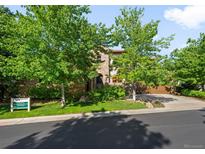 Stone home featuring mature trees, a lush lawn, and a driveway leading to an attached two-car garage at 9151 E Harvard Ave, Denver, CO 80231