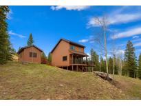 Beautiful cabin-style home with wood siding and a covered deck, nestled on a hill with surrounding trees at 33606 Gap Rd, Golden, CO 80403