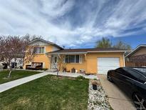 Charming yellow home featuring a well-manicured lawn and a driveway with a black car at 14595 Robins Dr, Denver, CO 80239