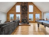 Spacious living room boasts wood paneling, stone fireplace, and ample natural light from multiple windows at 31551 Black Widow Dr, Conifer, CO 80433