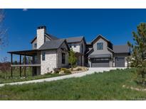Beautiful exterior view of home featuring stone accents, attached garage, and covered deck on a sprawling green lawn at 2442 Fox View Trl, Franktown, CO 80116