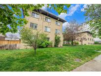 Charming brick apartment building surrounded by lush green lawn and mature trees under a bright sky at 665 Washington St # 5B, Denver, CO 80203