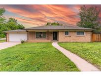 Charming brick home featuring a manicured lawn, walkway and an attached garage with a beautiful sky at 7995 Robin Ln, Denver, CO 80221
