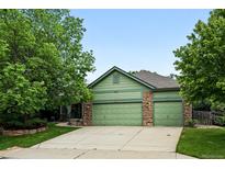Green home featuring a three-car garage with stone accents and mature trees in a well-maintained yard at 2130 Chestnut Cir, Erie, CO 80516