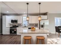 Modern kitchen with white cabinets, stainless steel appliances, granite countertops, and stylish pendant lighting over an island with seating at 530 Hickory St, Hudson, CO 80642