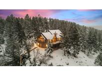 Stunning exterior view of cabin-style home nestled amongst the snowy forest at dusk at 6530 Ridgeview Dr, Morrison, CO 80465
