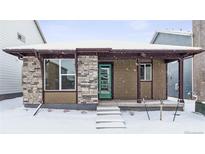 Snow-covered exterior of charming craftsman home with covered porch and teal door at 2763 Optimista Pl, Brighton, CO 80601
