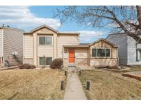 Charming tan two-story home with an orange front door and a well-manicured lawn with mature trees at 4314 Nepal St, Denver, CO 80249