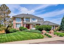 Charming brick home featuring a manicured lawn, brick stairs and pillars, and a red front door at 15573 E Prentice Ln, Centennial, CO 80015