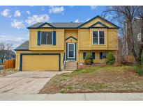 Charming two-story home with a bright yellow exterior, blue trim, and a two-car garage at 10241 Routt St, Broomfield, CO 80021