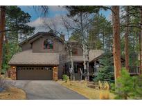 Stunning exterior of home with a three car garage, stone accents, and mature trees at 31332 Island Dr, Evergreen, CO 80439