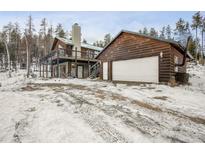 Log home with attached garage and deck, nestled in a snowy wooded area at 721 Aspen Way, Evergreen, CO 80439