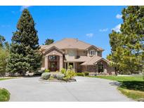 Stunning home featuring manicured lawn, circular driveway, brick accents and mature trees under a blue sky at 7645 Fox Creek Trl, Franktown, CO 80116