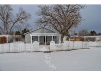 Gray house with white picket fence, covered porch, and snowy yard at 6355 W Jefferson Pl, Lakewood, CO 80226