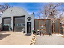 Unique Quonset-style home featuring an arched roof, garage doors, artistic details, and decorative fencing at 410 Goodrich Ave, Platteville, CO 80651