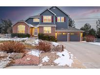 Charming two-story home with brick and siding, a three-car garage and beautifully landscaped front yard with snow at 2402 W Dry Creek Ct, Littleton, CO 80120