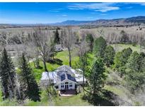 Stunning aerial view of a white home with solar panels, green lawn, mature trees, and mountain views at 9445 Lykins Pl, Longmont, CO 80503