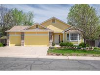 Charming yellow home featuring an attached garage and beautifully landscaped front yard at 1606 Iris St, Broomfield, CO 80020
