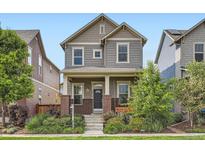 Charming two-story home featuring gray siding, brick accents, landscaped yard, and welcoming front porch at 10479 E 25Th Dr, Aurora, CO 80010