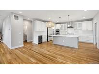 Bright, open kitchen featuring white cabinets, stainless steel appliances, an island, and wooden floors at 779 Kohlor Dr, Lafayette, CO 80026