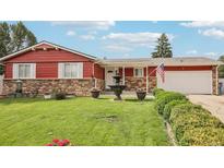 Charming red single-story home featuring a well-manicured lawn, stone accents, and a decorative water fountain at 14791 E Security Pl, Aurora, CO 80011
