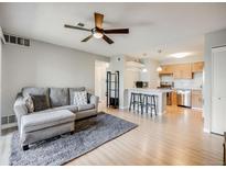 Bright living room featuring modern ceiling fan, plush gray sofa, and open access to the kitchen area at 2575 S Syracuse Way # K201, Denver, CO 80231