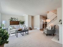 Bright living room features plush carpeting, a stylish sofa, and modern decor with a fireplace and staircase at 9057 E Oxford Dr, Denver, CO 80237