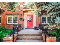 Charming red brick condo entrance with a vibrant red door, surrounded by lush greenery and decorative plants at 1365 N Corona St # 11, Denver, CO 80218