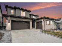 Modern home boasting a three car garage, sleek gray siding, and decorative stone accents against a vibrant sunset sky at 6429 Stable View St, Castle Pines, CO 80108