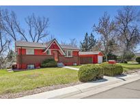Charming red and brick home with lush green lawn and mature trees on a sunny day at 10978 W Ada Pl, Lakewood, CO 80226