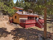 View of the exterior with a large deck, beige siding, and red trim surrounded by trees at 10852 Conifer Mountain Rd, Conifer, CO 80433