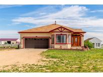 Tan home with brown garage door and red trim nestled on a sprawling green lawn with blue skies above at 46303 E 106Th Ave, Bennett, CO 80102