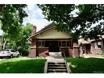Charming brick home featuring a welcoming front porch, lush lawn, and mature trees at 723 Steele St, Denver, CO 80206