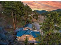 Stunning mountain home with a blue roof nestled amongst evergreen trees against a colorful sky at 20951 Pleasant Park Rd, Conifer, CO 80433